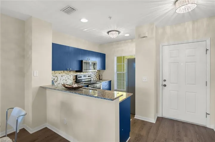 Kitchen featuring kitchen peninsula, appliances with stainless steel finishes, dark stone counters, blue cabinetry, and dark hardwood / wood-style floors