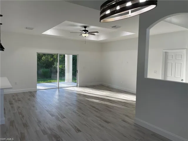 Empty room with hardwood / wood-style floors, ceiling fan, and a tray ceiling