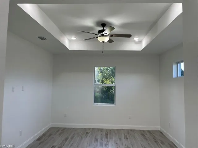Empty room featuring ceiling fan, plenty of natural light, light hardwood / wood-style flooring, and a tray ceiling