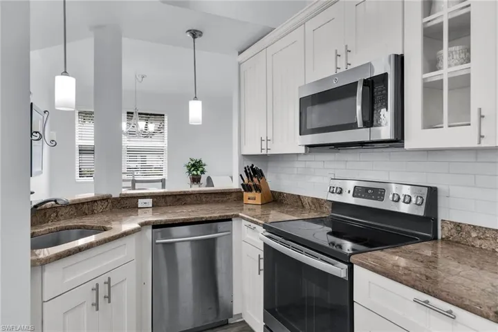 Kitchen with stainless steel appliances, white cabinets, tasteful backsplash, dark stone counters, and decorative light fixtures