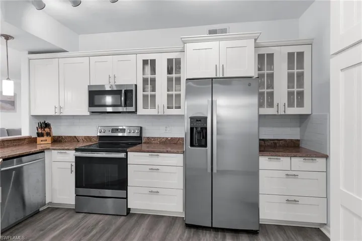 Kitchen featuring appliances with stainless steel finishes, tasteful backsplash, glass insert cabinets, and white cabinetry