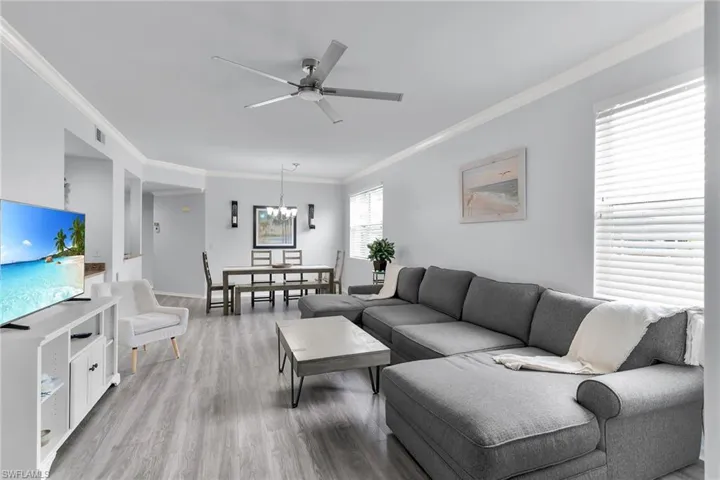 Living room featuring crown molding, light wood-style flooring, a ceiling fan, and a chandelier