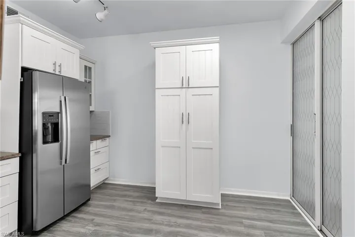 Kitchen with stainless steel refrigerator with ice dispenser, glass insert cabinets, light wood finished floors, white cabinets, and dark stone counters