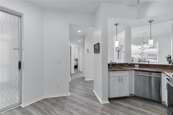 Kitchen featuring stainless steel appliances, light wood-style flooring, decorative light fixtures, a chandelier, and dark stone counters