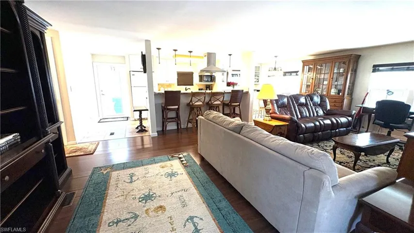 Open-concept living room with view to the entry. You’ll love the rich wood-finish flooring, kitchen island with pendant lighting, stainless steel range hood, and recessed lighting.