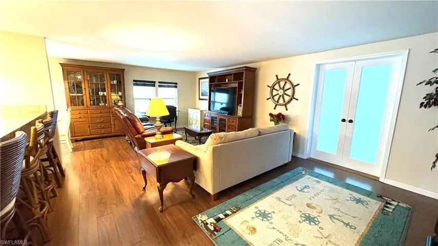 Expansive living area has beautiful wood-finish flooring, white baseboards, and light-toned walls. The double doors lead to the air-conditioned Florida Room.