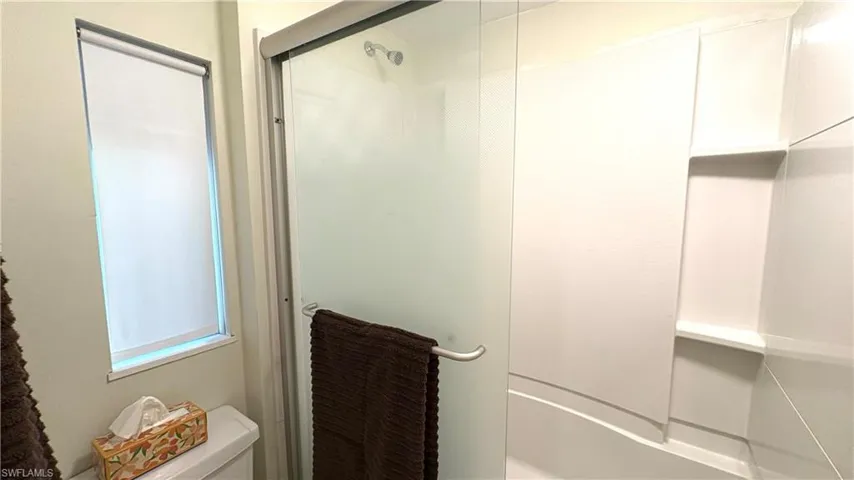 Primary bathroom has a shower-tub combination featuring a frosted glass enclosure and integrated shelving
