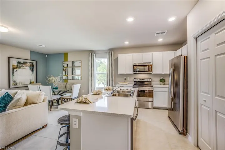 Kitchen with a kitchen island with sink, a kitchen bar, sink, appliances with stainless steel finishes, and white cabinets