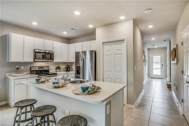 Kitchen with a breakfast bar area, light tile patterned floors, appliances with stainless steel finishes, an island with sink, and white cabinets
