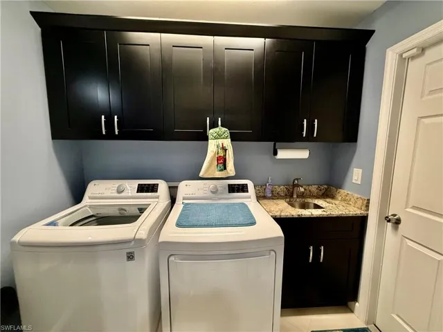 Indoor laundry area with cabinets and granite top on sink.