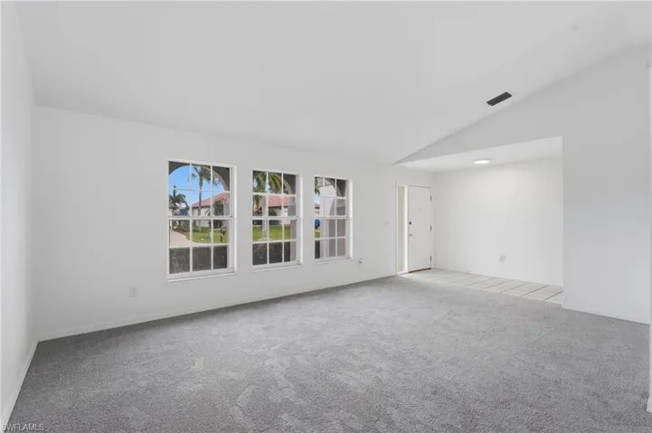 Spacious interior featuring three front-facing windows with arched accents, vaulted ceilings, and gray carpeting