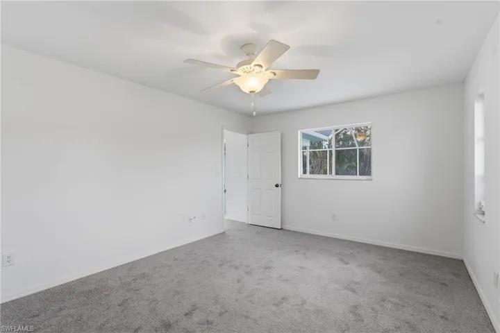 Spacious room featuring light gray carpeting, neutral wall finishes, a modern ceiling fan with integrated lighting, and a white interior door