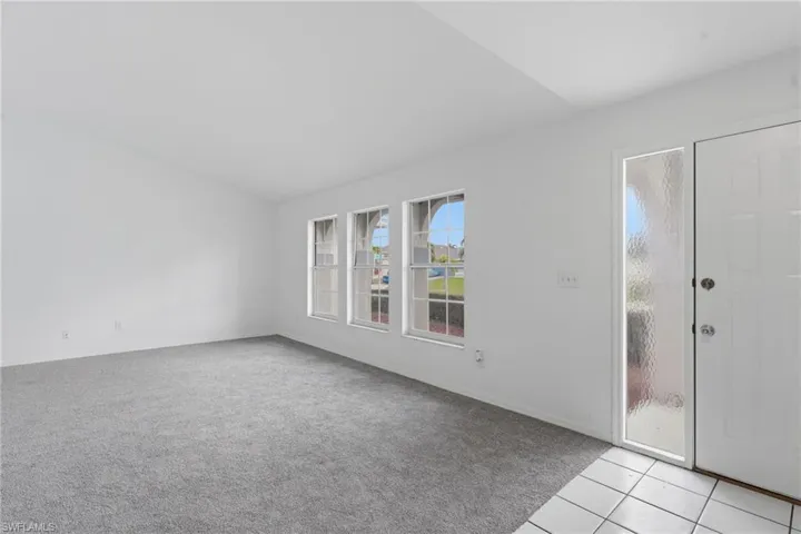 Carpeted living area with white walls and multiple windows