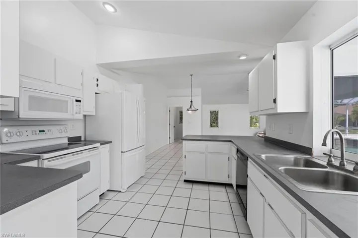 Spacious kitchen featuring white cabinetry, dark countertops, white tile flooring, stainless steel double basin sink, and white appliances