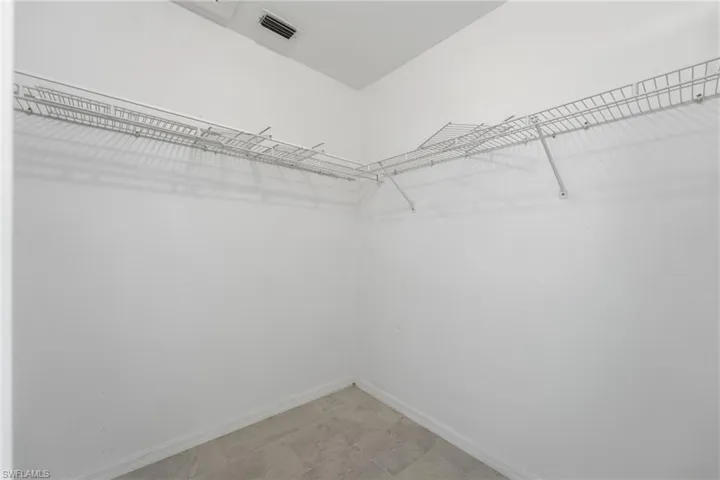 Corner closet featuring white wire shelving, light-toned tile flooring, white baseboards, and a ceiling vent