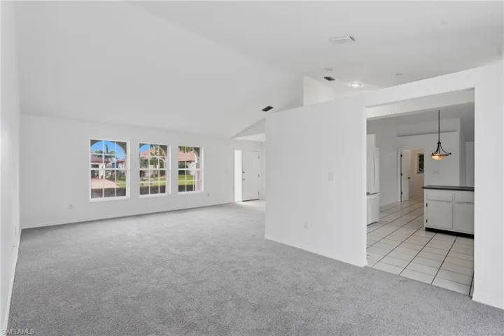 Spacious living area featuring vaulted ceilings, light gray carpet, and three large windows providing ample natural light