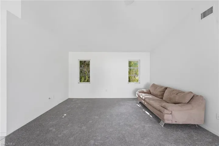 Spacious room featuring vaulted ceilings, neutral wall tones, gray carpeting, and two windows