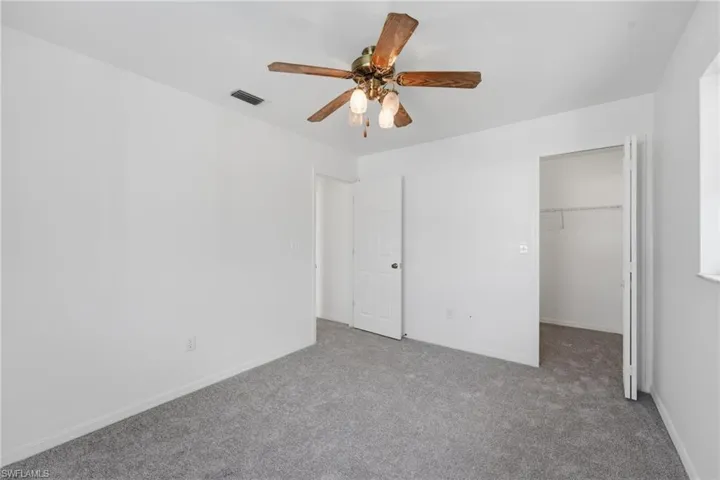 Carpeted room with white walls, a ceiling fan with light fixture, a window with a white sill, and a closet with wire shelving