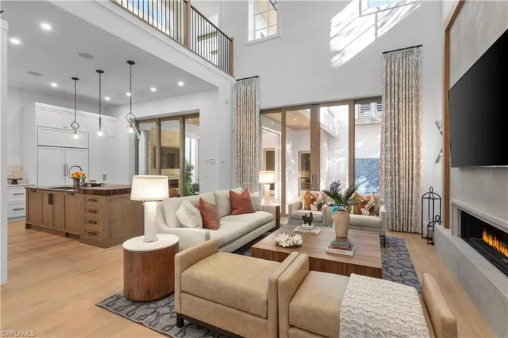 Living room featuring light wood-type flooring, a towering ceiling, a warm lit fireplace, and recessed lighting