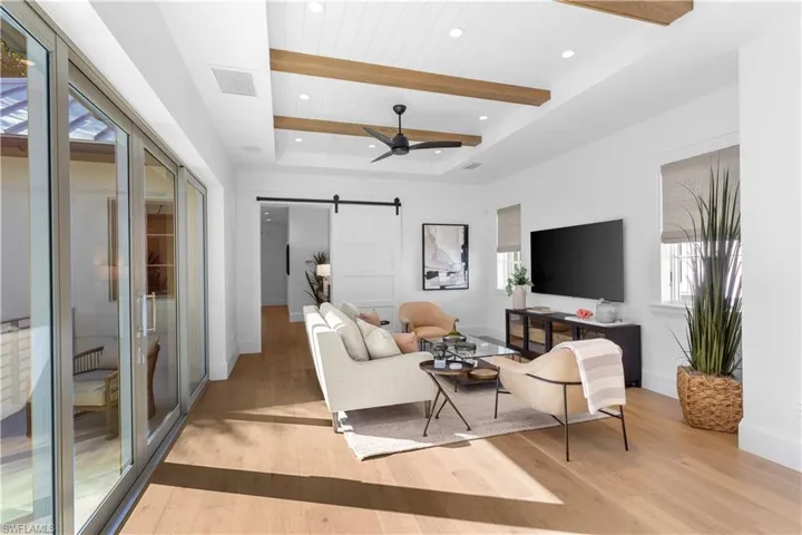 Living area with a barn door, light wood finished floors, baseboards, a ceiling fan, and a raised ceiling