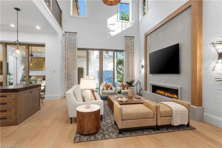 Living area featuring light wood-type flooring, a warm lit fireplace, a high ceiling, and baseboards