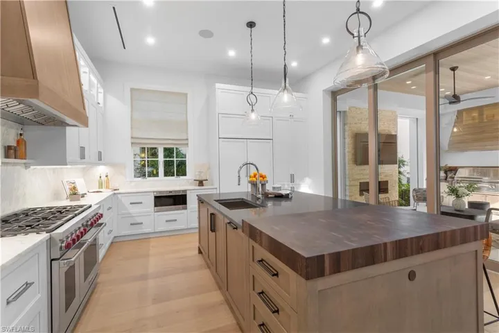 Kitchen featuring a sink, range with two ovens, backsplash, an island with sink, and custom exhaust hood