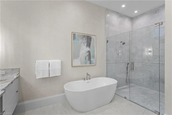 Bathroom featuring vanity, a freestanding tub, a stall shower, baseboards, and recessed lighting