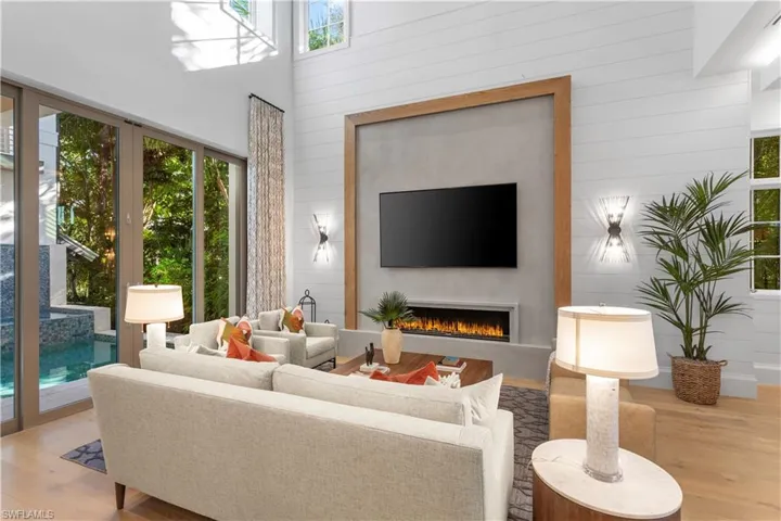 Living area with healthy amount of natural light, wood finished floors, a warm lit fireplace, wood walls, and a high ceiling