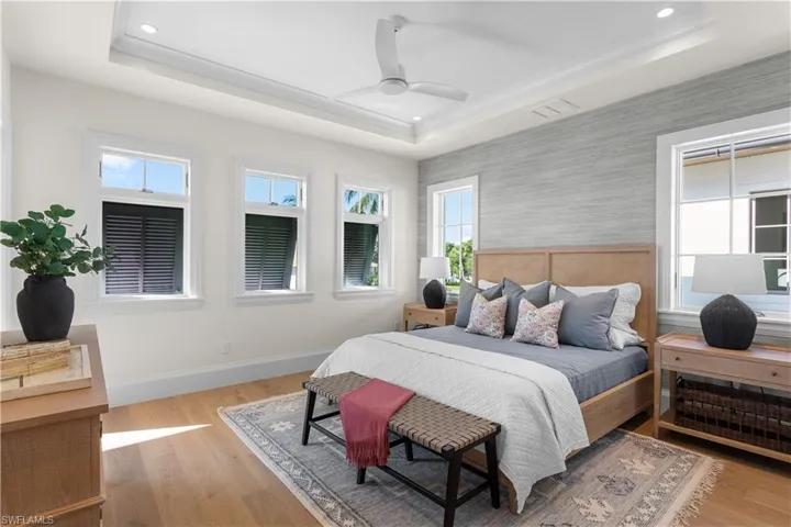Bedroom featuring a tray ceiling, wallpapered walls, recessed lighting, baseboards, and wood finished floors