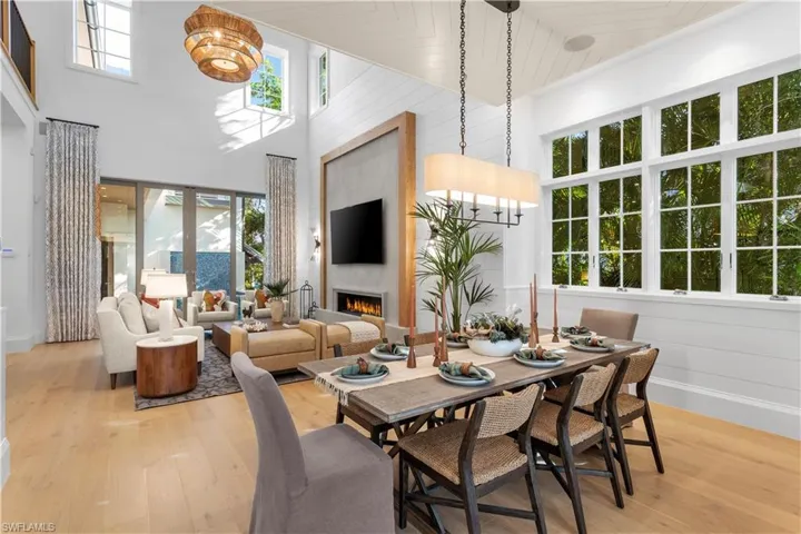 Dining room featuring a towering ceiling, light wood-style flooring, a lit fireplace, and baseboards