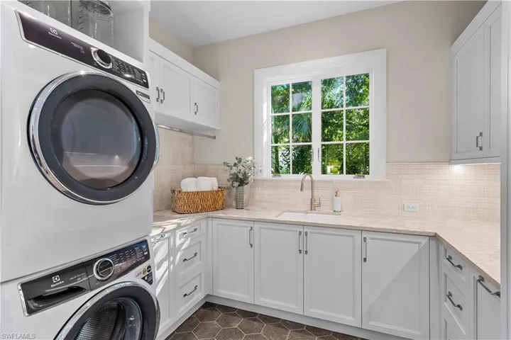 Laundry area featuring stacked washing machine and dryer, cabinet space, and dark tile patterned floors