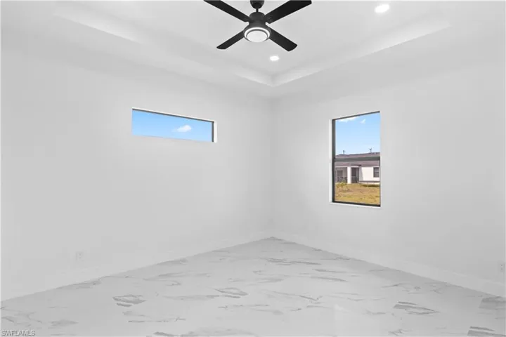 Empty room with light marble finish floors, a raised ceiling, healthy amount of natural light, and recessed lighting