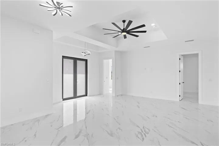 Empty room featuring a tray ceiling, light marble finish floors, a ceiling fan, french doors, and recessed lighting