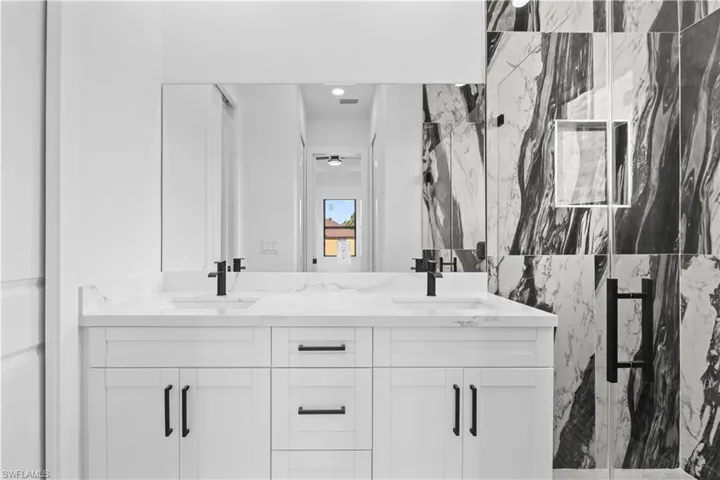 Full bath with a marble finish shower and double vanity