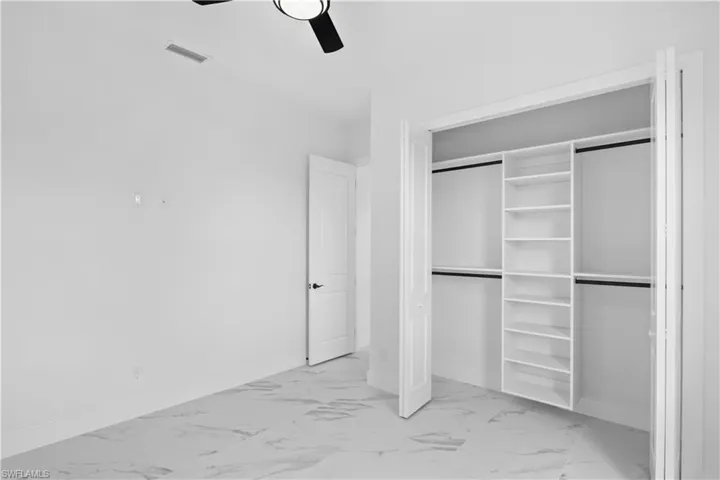 Unfurnished bedroom featuring light marble finish floors, a closet, and a ceiling fan