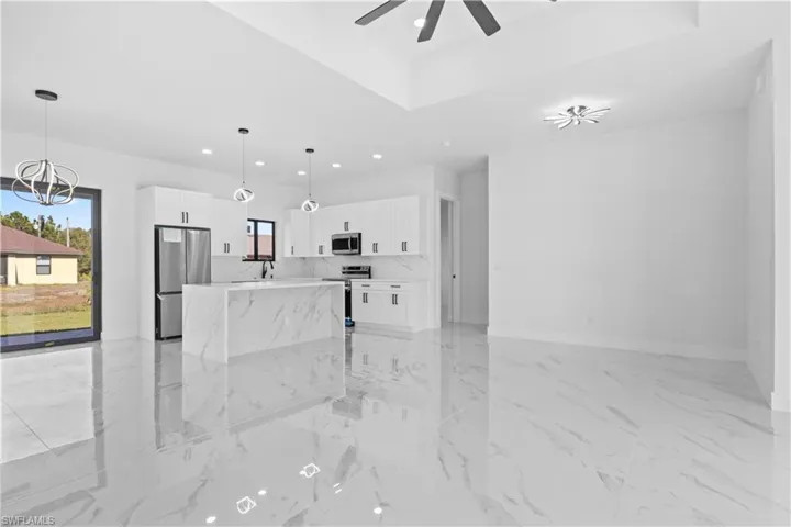 Unfurnished living room featuring light marble finish floors, recessed lighting, a chandelier, a tray ceiling, and ceiling fan