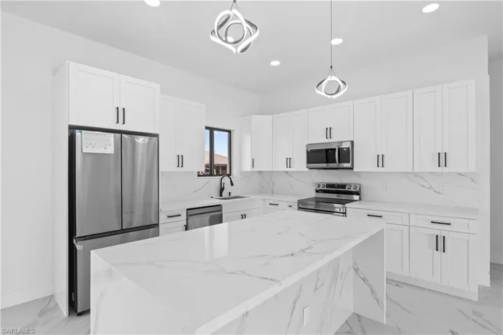 Kitchen with light stone counters, stainless steel appliances, pendant lighting, recessed lighting, and white cabinets