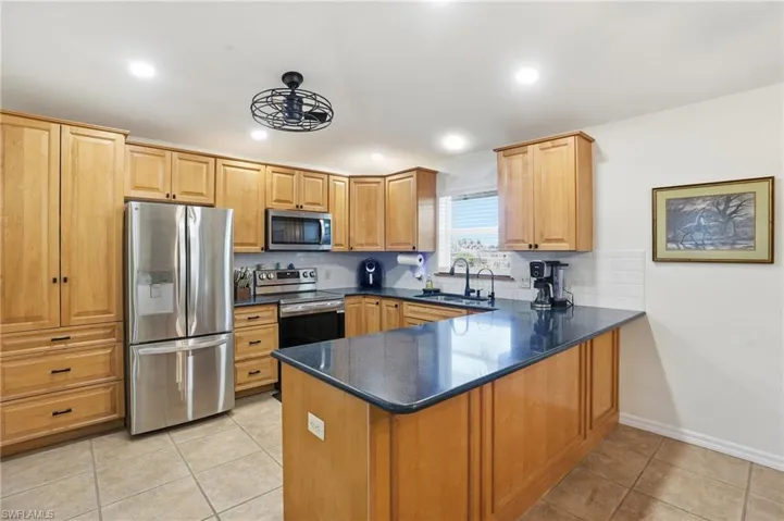 Kitchen with stainless steel appliances, light tile patterned flooring, a peninsula, dark stone countertops, and light brown cabinets