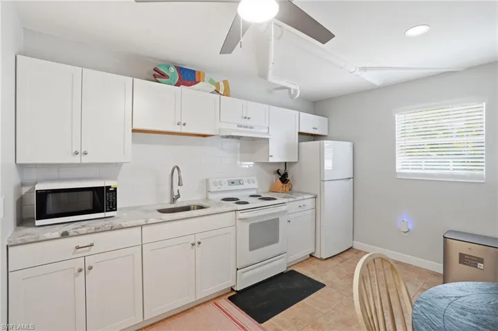 Kitchen featuring white appliances, white cabinets, a ceiling fan, decorative backsplash, and under cabinet range hood
