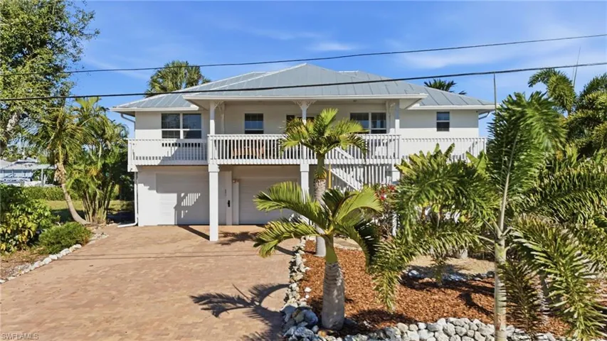 Beach home with a metal roof, a balcony, decorative driveway, a garage, and stairs