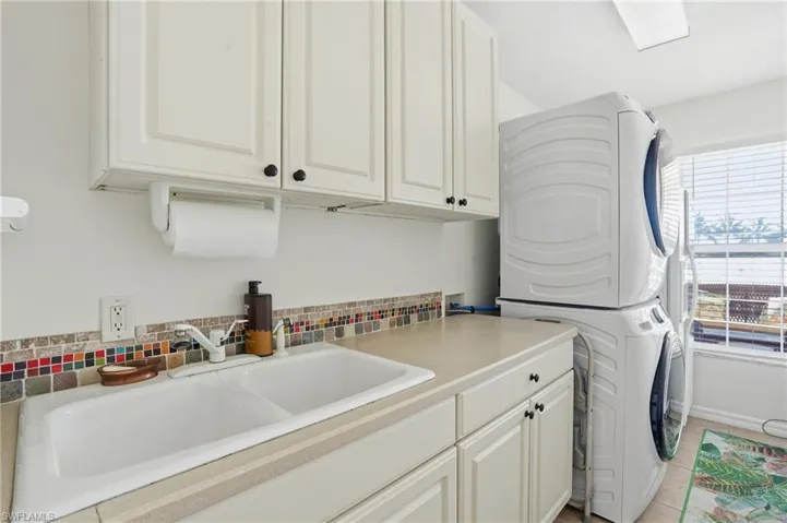 Laundry room with stacked washing machine and dryer, cabinet space, and light tile patterned floors