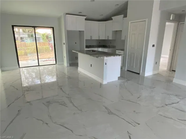 Kitchen featuring dark stone counters, a center island, white cabinets, light tile floors, and lofted ceiling