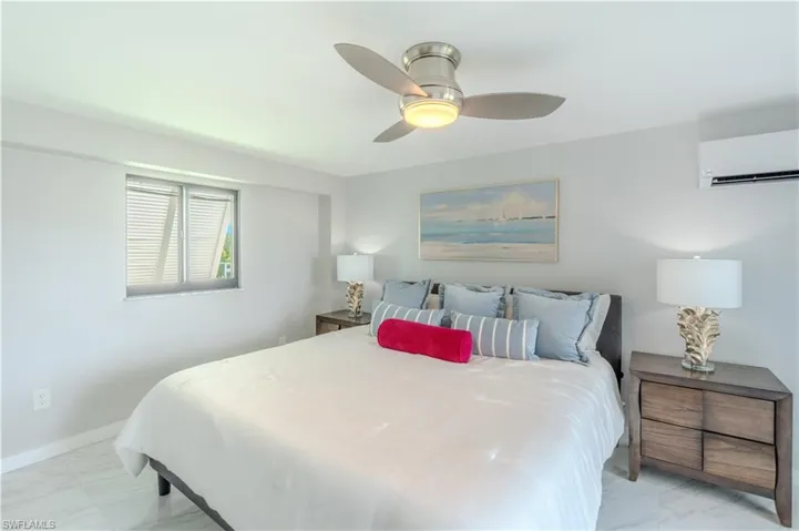 Bedroom with light marble finish floors, a wall mounted AC, and ceiling fan - Virtually Edited Image