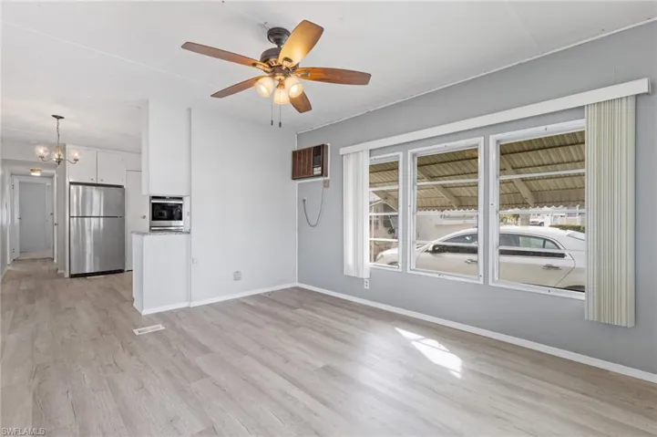 Unfurnished living room with an AC wall unit, ceiling fan with notable chandelier, and light wood-type flooring