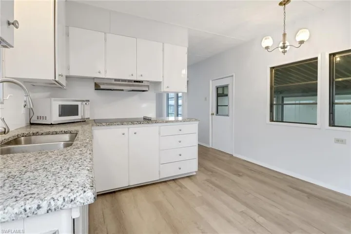 Kitchen with white cabinets, sink, light hardwood / wood-style flooring, decorative light fixtures, and a chandelier