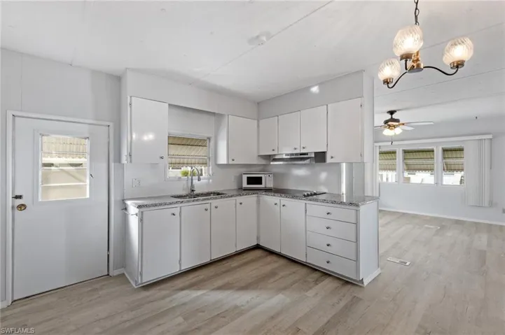 Kitchen with white cabinets, ceiling fan with notable chandelier, pendant lighting, and sink