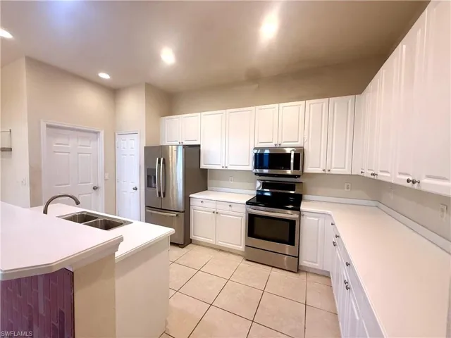 Kitchen with stainless steel appliances, oversized refrigerator with in door ice maker, light countertops, white cabinets, light tile patterned floors, and an island with sink