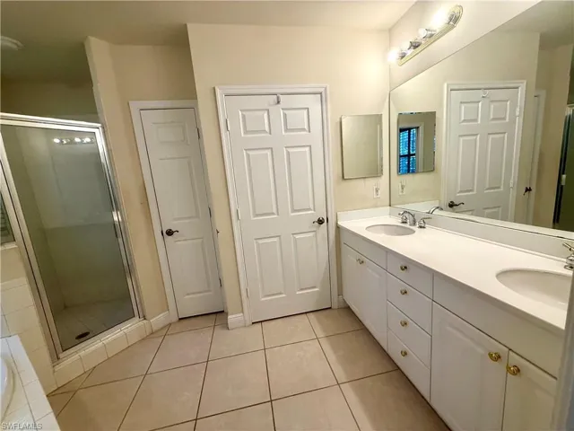 Primary Bath has separate walk in stall shower, double vanity, water closet with wooden shelving, separate powder room, light tile patterned flooring, and a garden soaking tub