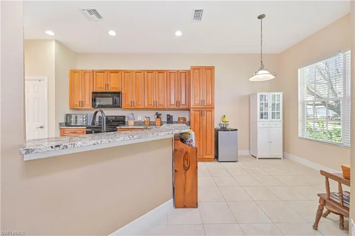 Kitchen with wood finish cabinets, light stone counters, black appliances, pendant lighting, and light tile patterned flooring