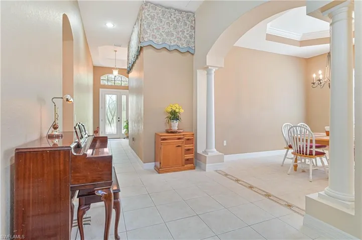 Foyer with light tile patterned floors, ornate columns, arched walkways, a chandelier, and a raised ceiling